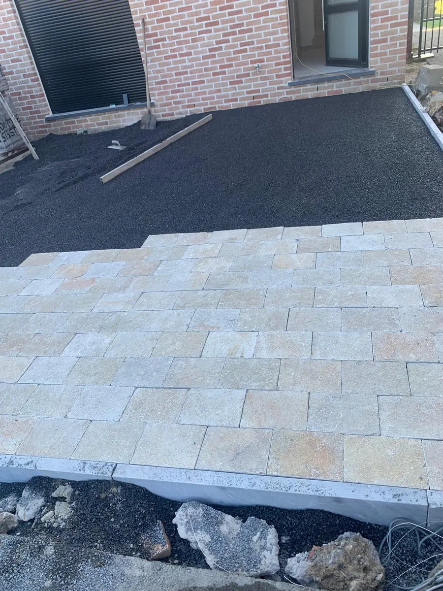 Beige natuursteen kasseien geplaatst op zwart legbed voor een terras