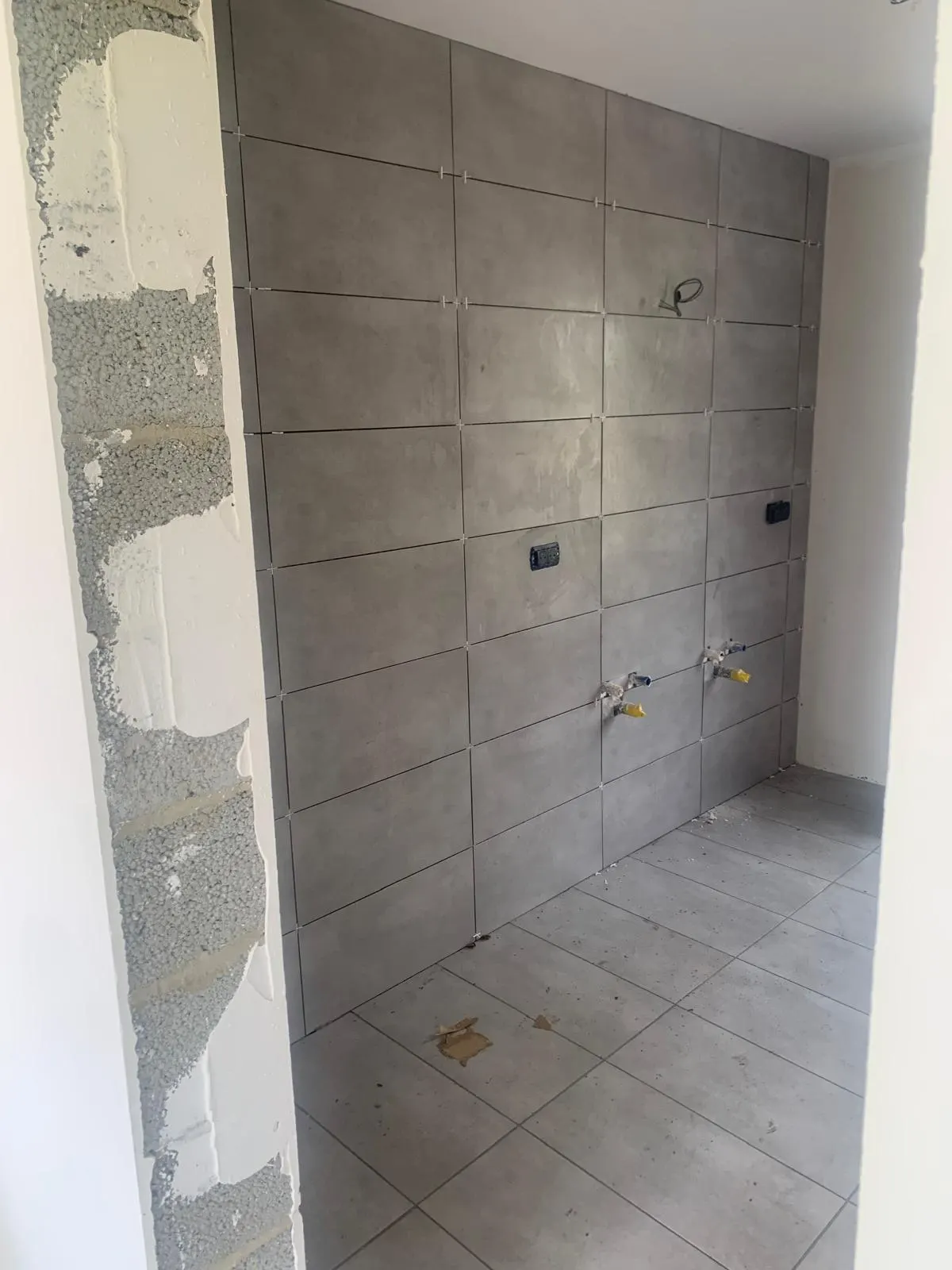 Shower wall in grey concrete-effect tiles with plumbing outlets prepared
