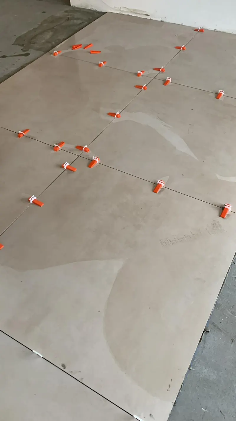 Large beige tiles held by orange levelling system during installation