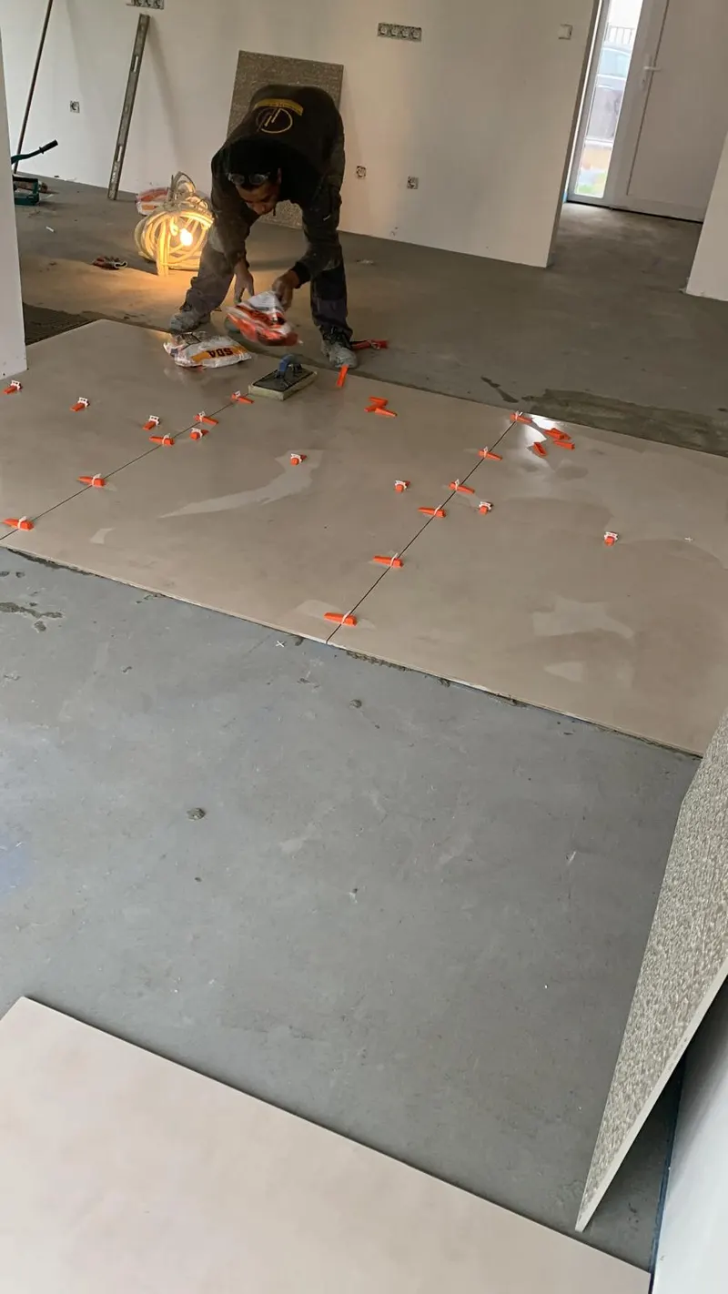 Tiler laying large beige floor tiles on a screed