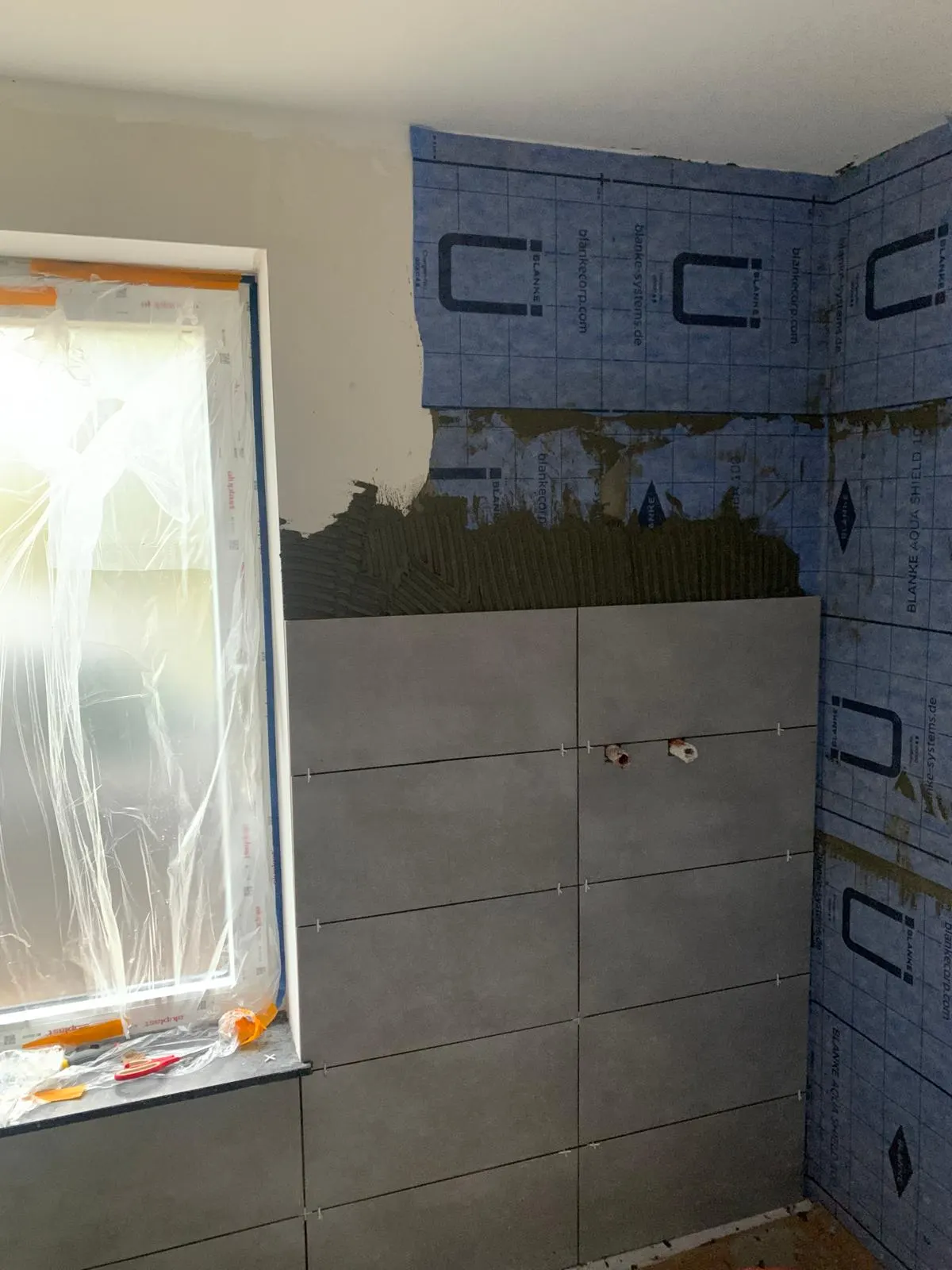 Carreaux muraux gris effet béton posés sur natte d'étanchéité en salle de bain