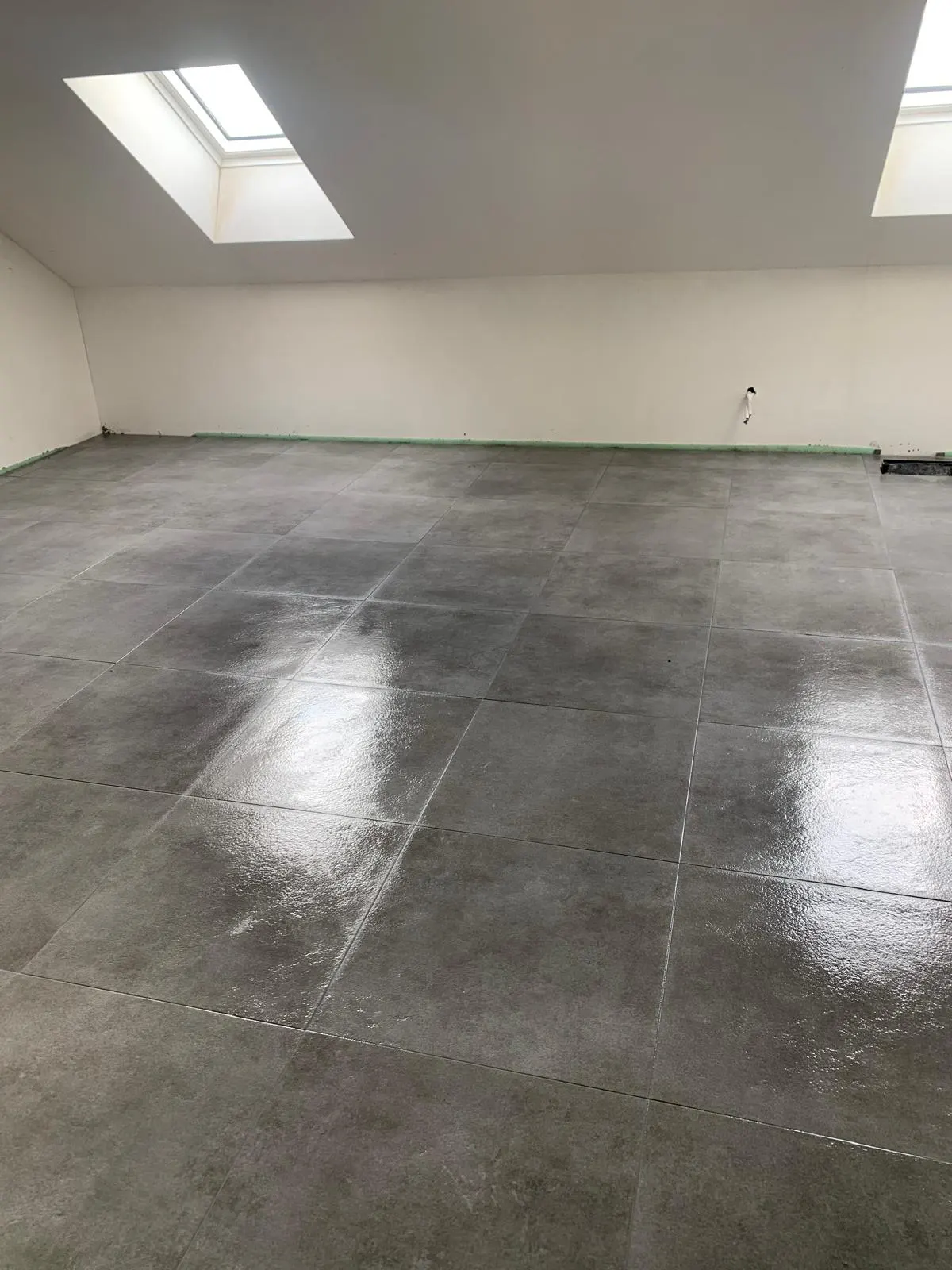 Grijze betonlook vloer in een zolderruimte met dakramen