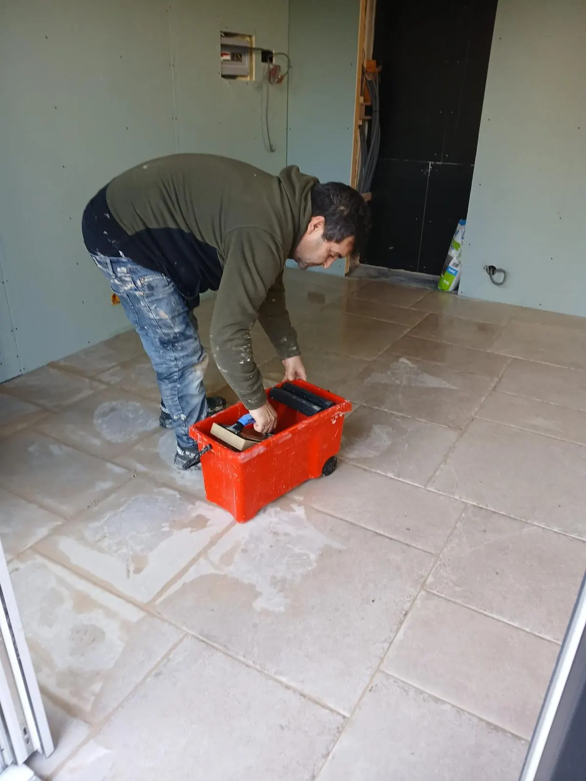 Tegelzetter reinigt de voegen van een beige steenlook vloer