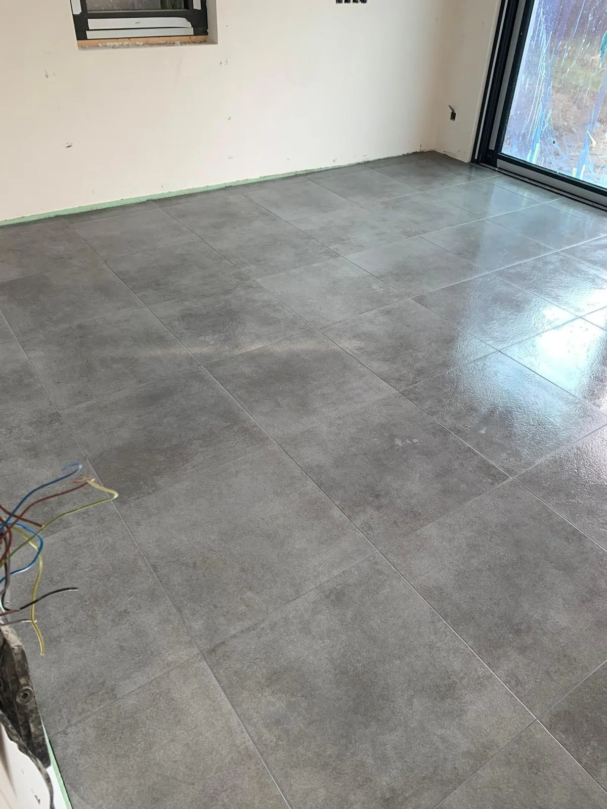 Vloer in grijze keramische tegels met betonlook groot formaat in een nieuwbouwruimte