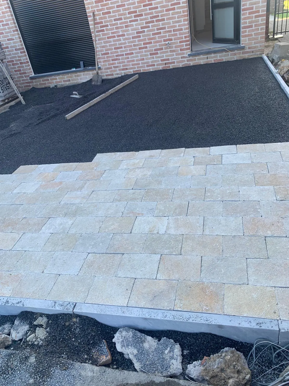 Beige natuursteen kasseien geplaatst op zwart legbed voor een terras